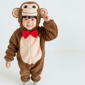 A smiling child in a brown plush monkey costume with a red bow tie stands against a white background.