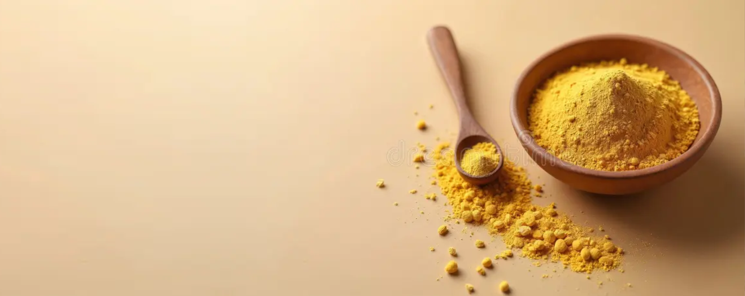 A wooden bowl and spoon with bright yellow turmeric powder.