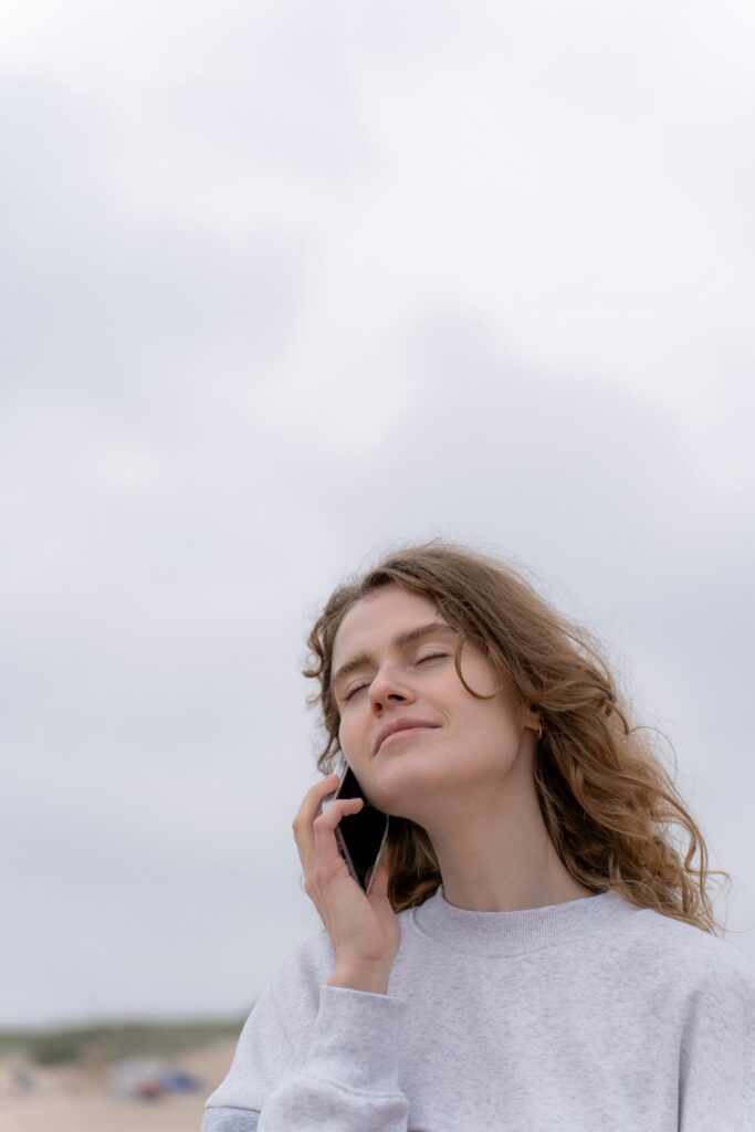 A young woman with a calm expression talking on her phone on a beach.